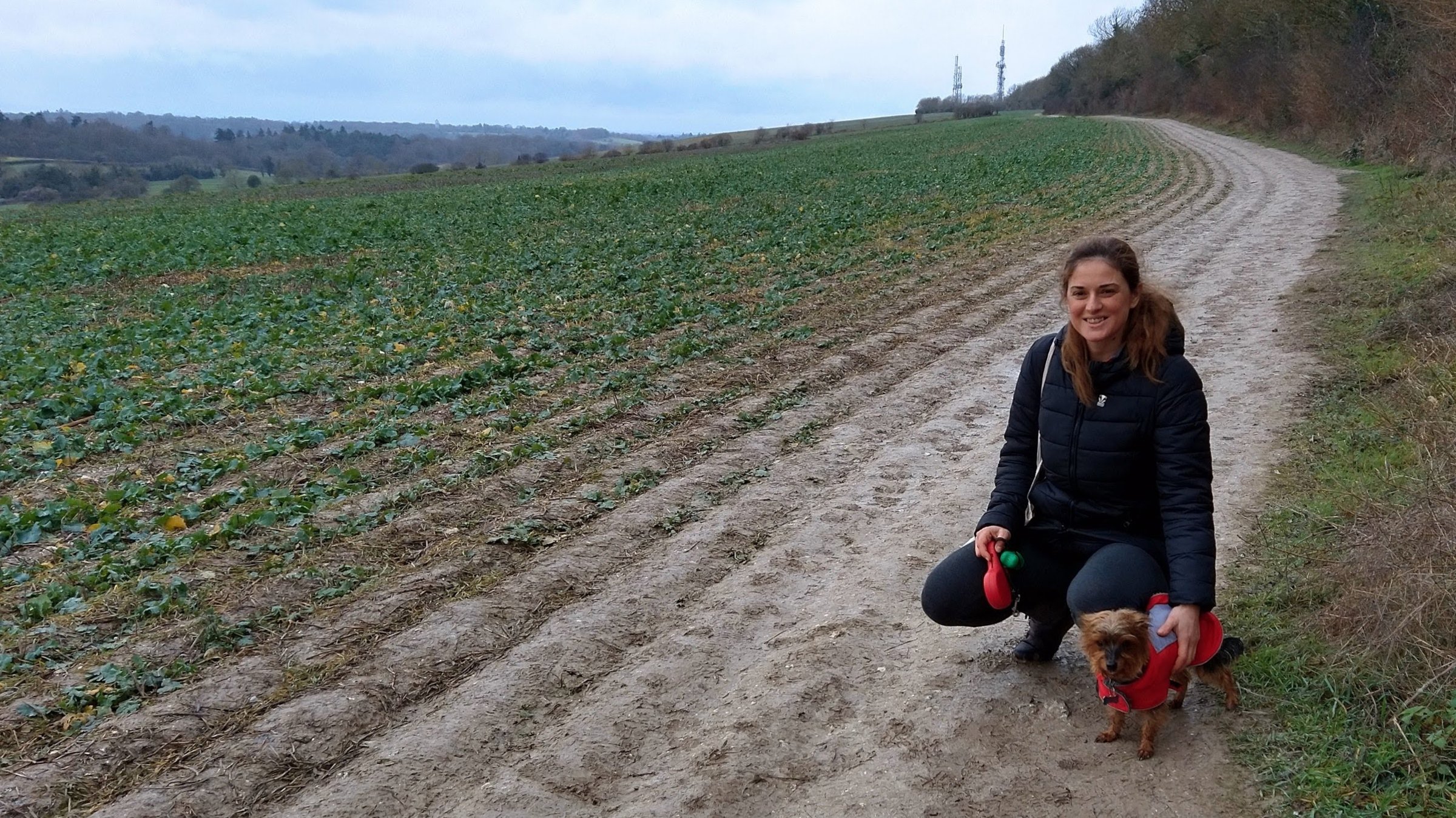 Maja walking a small dog on a track in the Surrey Hills, green fields and wooded hills beyond